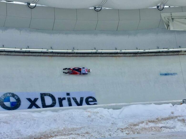 A man in a white and red bodysuit lies on his back on a luge sled as he races down a track.