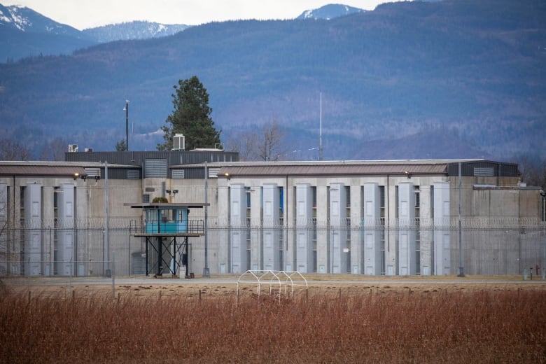 A concrete prison with a blue watch tower in front of it. In the distance are many mountains. 