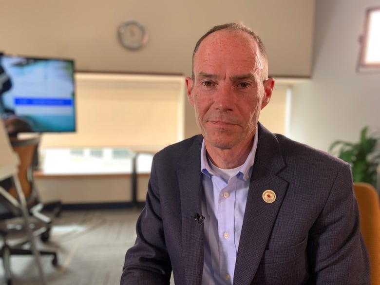 A man in a blue collared shirt with a suit jacket. He's sitting in a chair in an office setting.