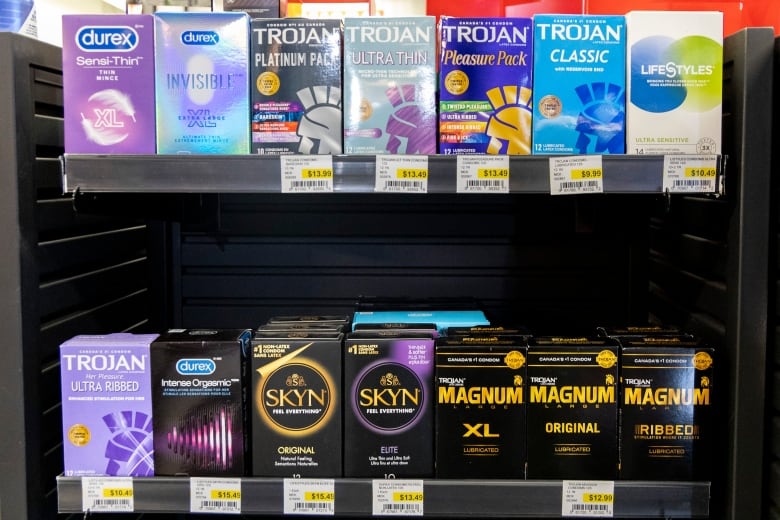 The condom section at a downtown Toronto Pharmasave store.  The shelf is mostly  full of the Trojan brand, with features an iconic warrior head silhouette graphic. 