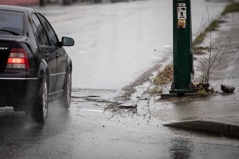 A car is pictured running on a wet road, with a power pole on the pavement.