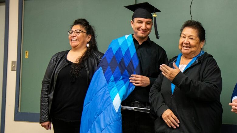 A man wearing a grad cap and star blanket receives his diploma.