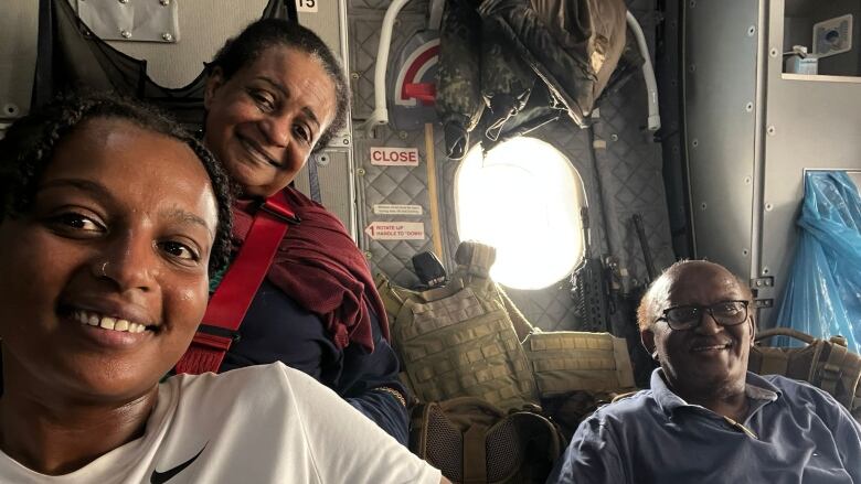 Two women and a man smile at a photo inside of aircraft.