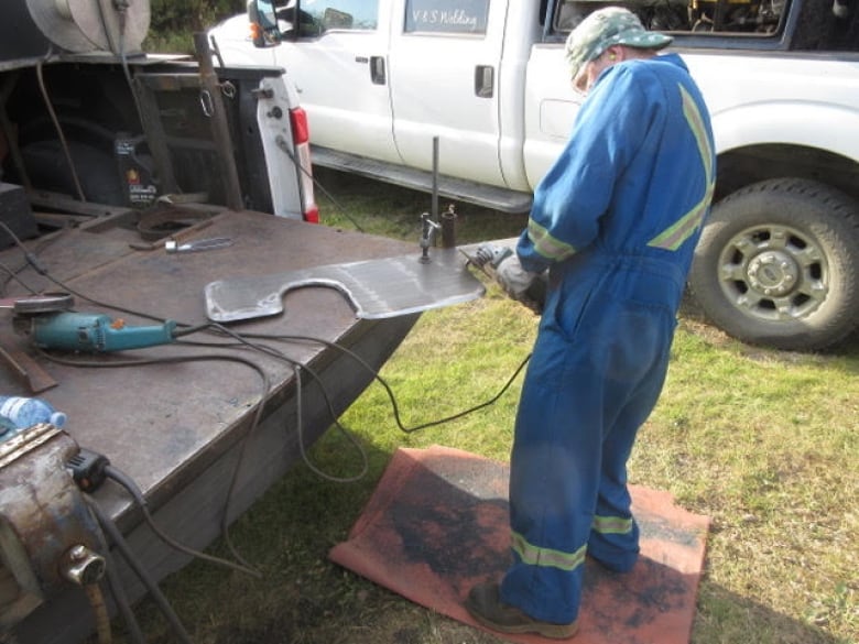 A man sands down a piece of metal sitting in the back of a truck.