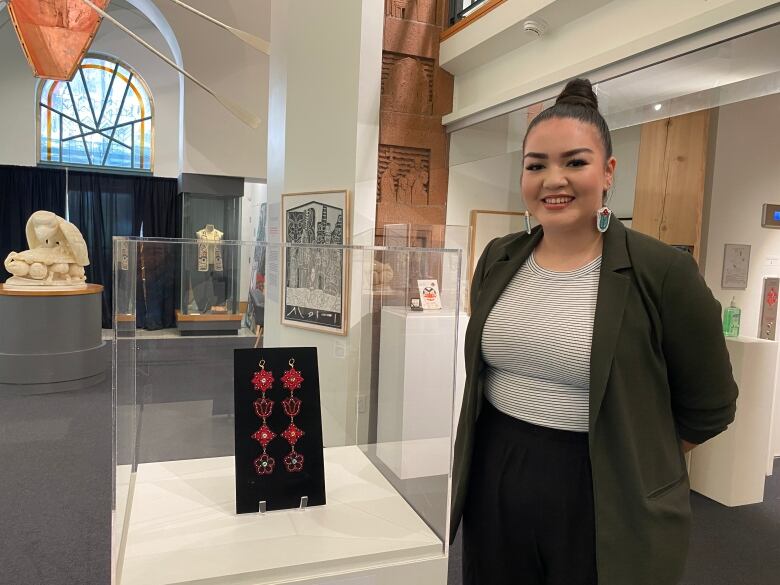 Woman stands beside glass display with red beaded earrings inside. 