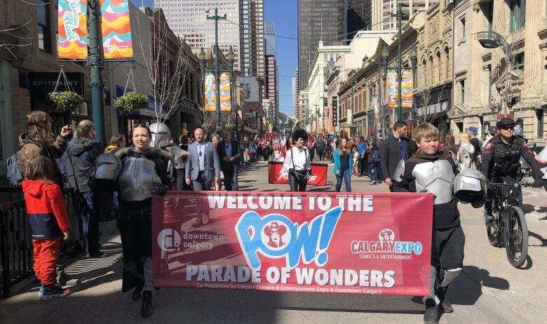 People carrying a banner for the POW! Parade of Wonders followed by the mayor walk in the parade.