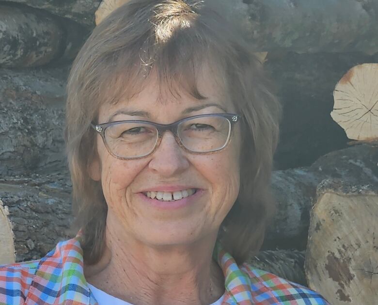 A woman smiling in front of piles of logs