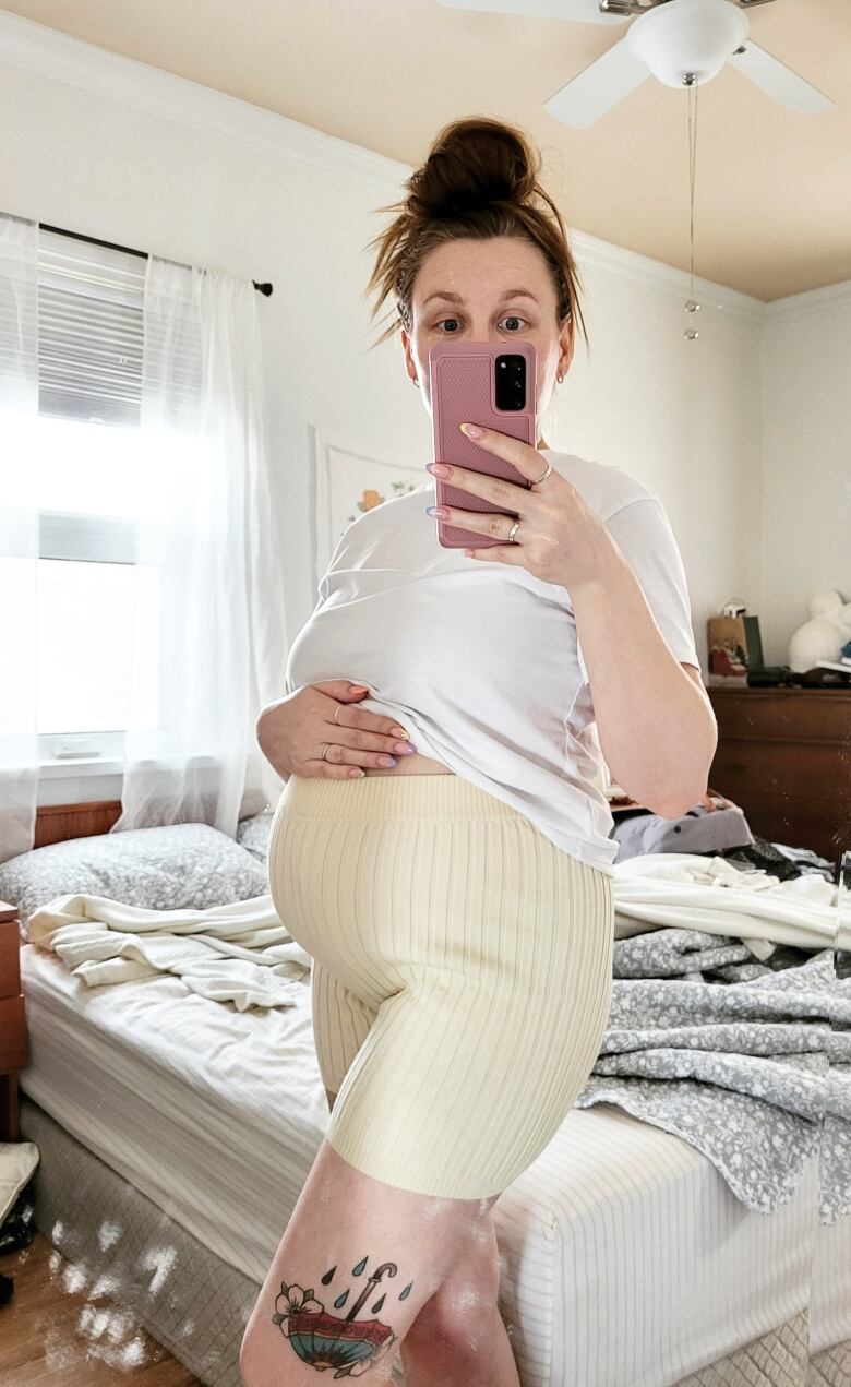 A pregnant woman wearing a medical mask takes a selfie in a mirror.