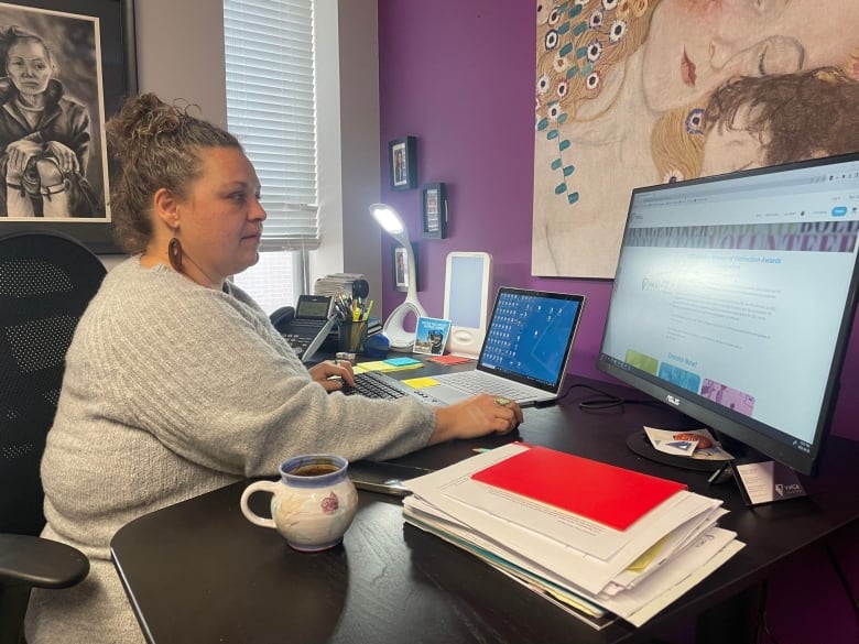 A woman in a grey sweater works on her computer. 