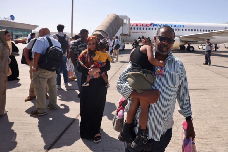 A couple carry two small children as they walk on an airport tarmac.