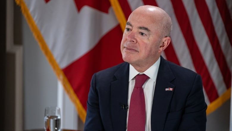 A man in a dark suit and red tie answers a question during an interview.