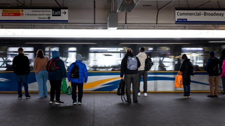 A number of people wait for a train at a public transit station.