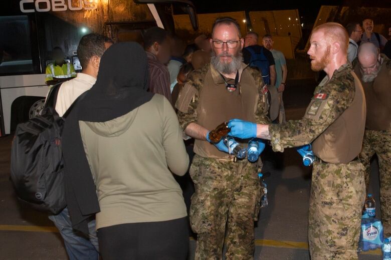 Soldiers and citizens stand near a bus.