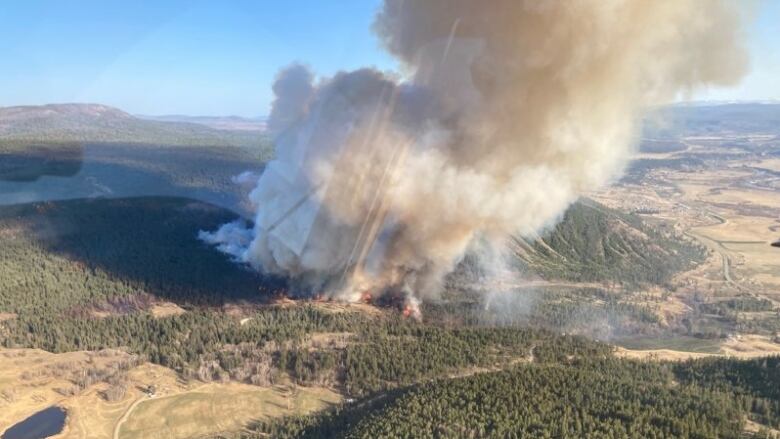 An aerial shot of a massive plume of smoke rising from forest-covered hills.