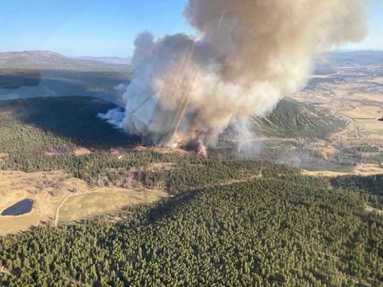 An aerial shot of a massive plume of smoke rising from forest-covered hills.