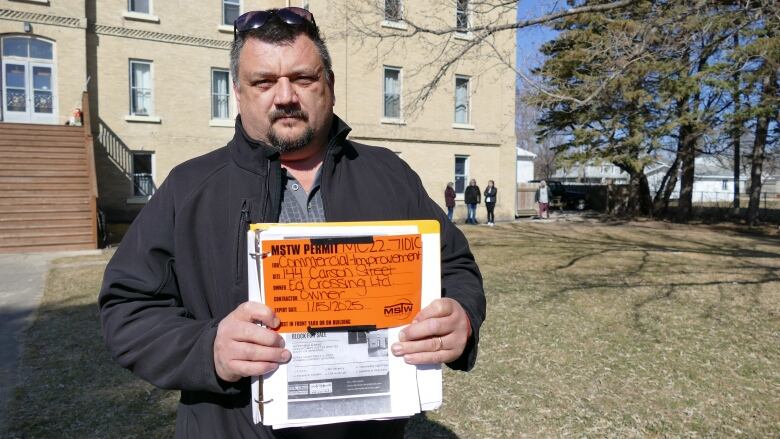 A man holds a binder with a bright orange building permit that reads 