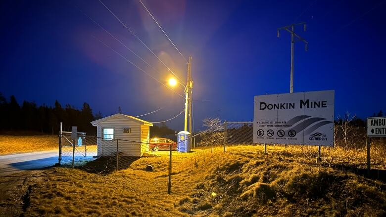 A yellow light illuminates the guard house at the entrance to a coal mine at night.