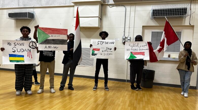 A group of teens holding flags and signs in support of Sudan are shown.