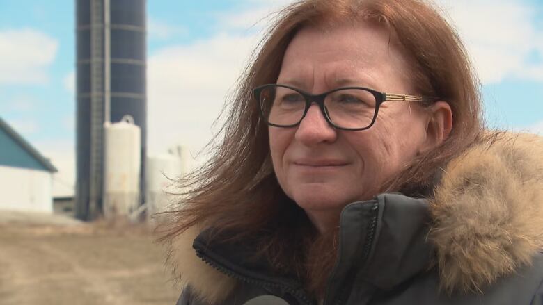 A woman wearing black glasses and a black coat stands in a field. 