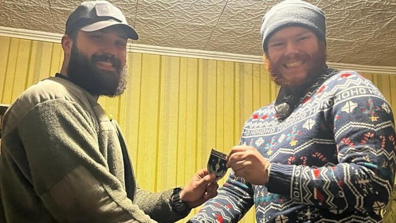 Two men wearing beards and hats smile and shake hands.