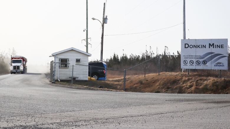 A truck drives along a dusty road heading towards a gated entrance where a sign says Donkin mine.