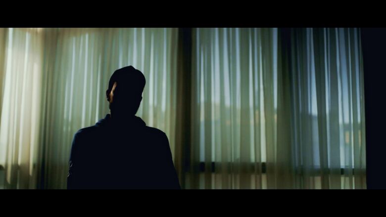 Silhouette of a man  in a curtained room, his face obscured in shadows.