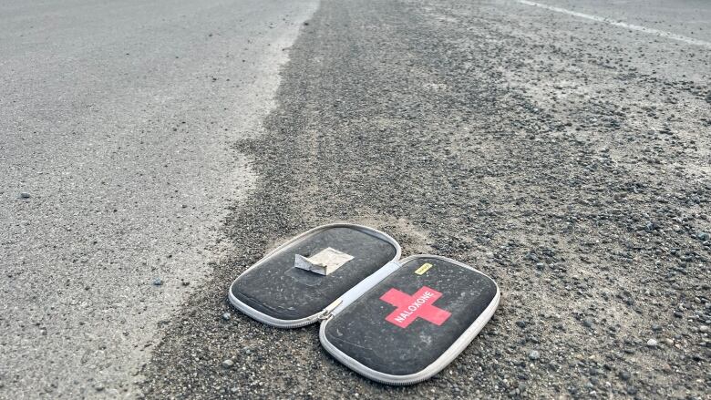 A used Naloxone kit is seen discarded on a city street.