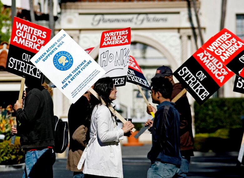 Several people are shown walking and carrying signs in an outdoor photo.