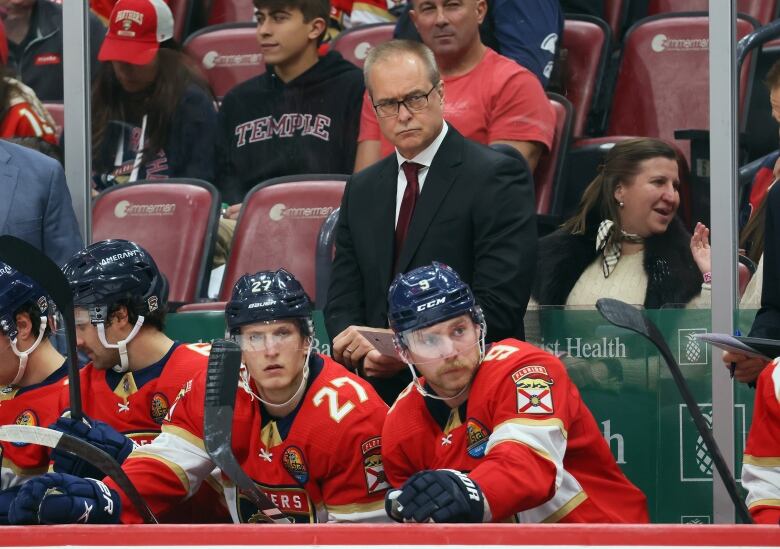 A hockey coach stands behind his players on the bench.