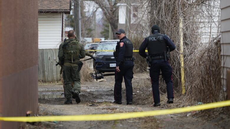 Three police officers in tactical gear walk down an alleyway.