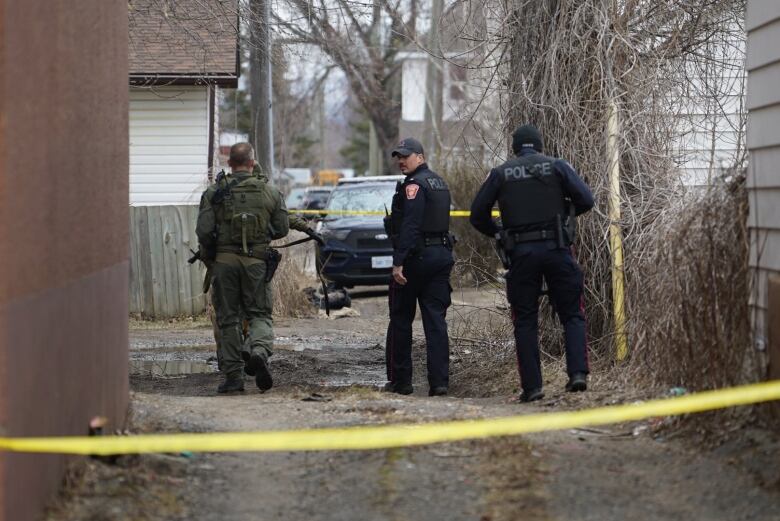 Three police officers in tactical gear walk down an alleyway.