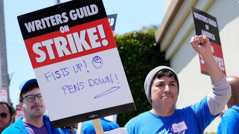 A man raises his fist with one hand and holds a strike sign in the other.