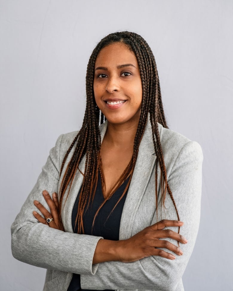 A woman smiles and crosses her arms while posing for a photo.