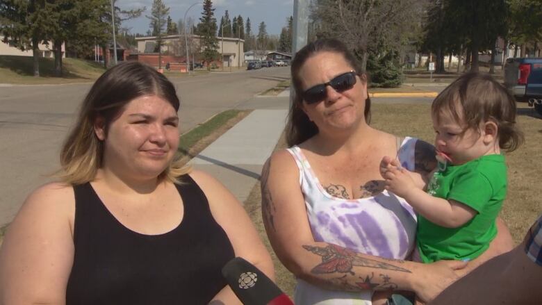 A younger and an older woman holding a baby, speak to CBC.