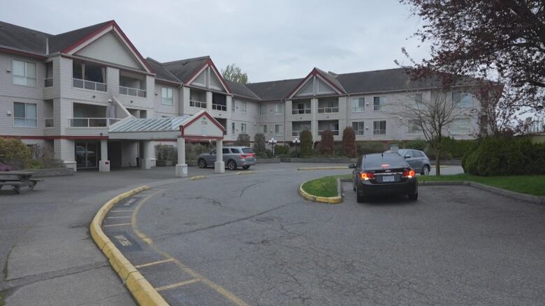 A three-storey apartment building with a long driveway stands with several cars parking in front of it.