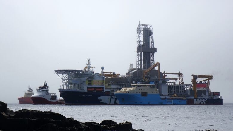 A large drilling ship sits in between three smaller vessels.