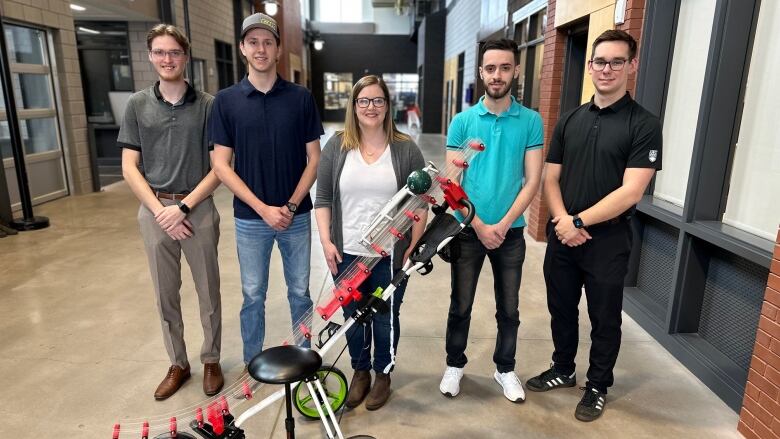 A group of engineering students and a volunteer with Special Olympics stand in front of a golf cart turned into a bocce ramp