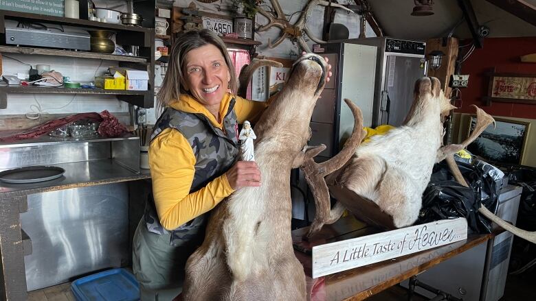 A woman stands in a room with two mounted caribou heads.