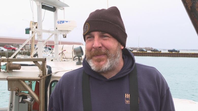 A bearded man stands on a wharf looking at the camera