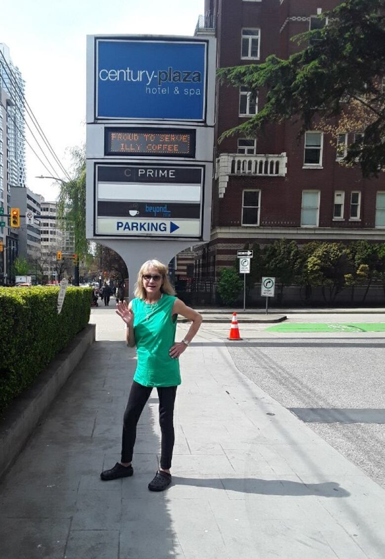 A woman in a green shirt and black leggings stands beside a sign that says 