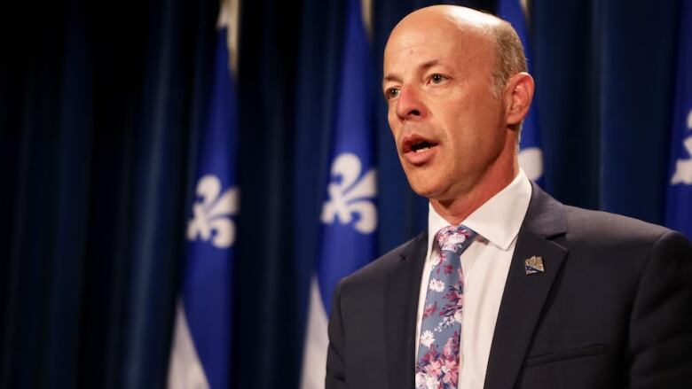 A man standing in front of Quebec flags speaks. 