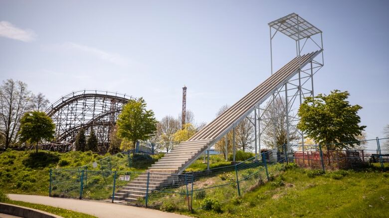 An art piece depicting a series of rising stairs is pictured behind blue fencing.