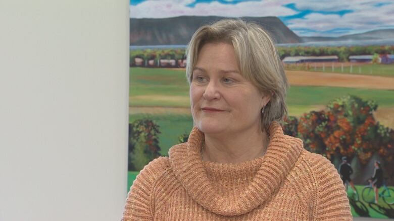 Woman wearing a pink sweater stands in front of a farm mural. 