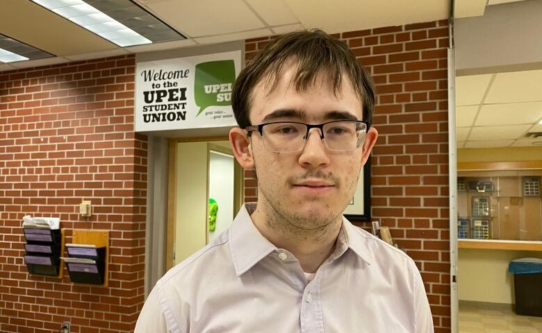 A man with glasses stands in an office with signage that reads: 