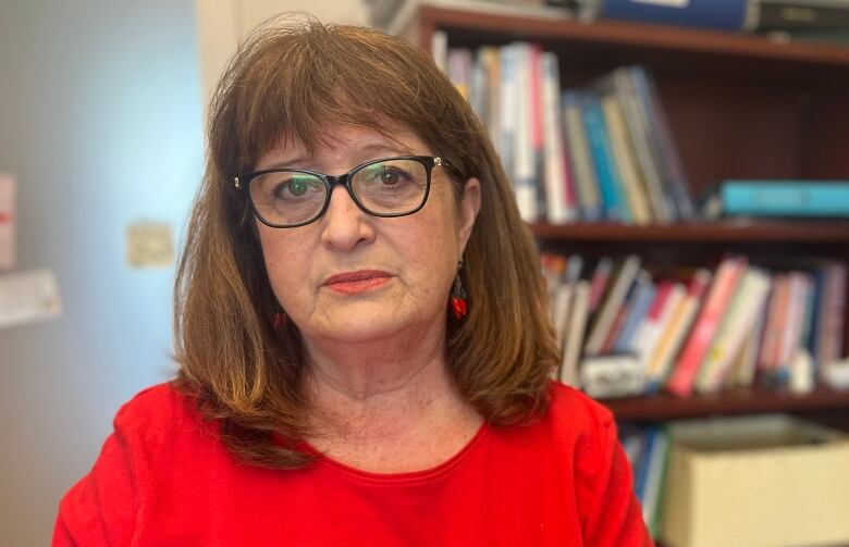 A brown haired woman with glasses stands in front of a bookshelf