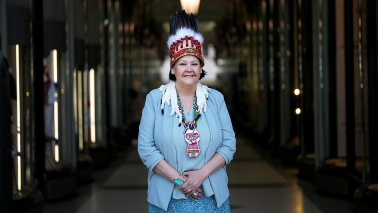 A woman wearing a feathered headdress smiles while standing in the hallway of a building.