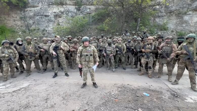 A man in a helmet and military fatigues is shown encircled by a number of troops in fatigues.