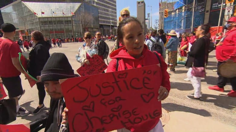 A woman in a red hoodie holds a red sign that says 