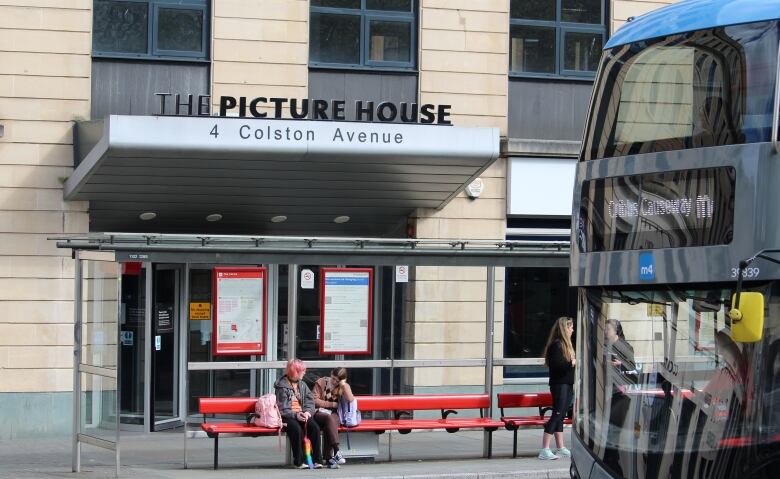 Two people sit on a red bench outside a building with the sign 'The Picture House,' at 4 Colston Avenue.