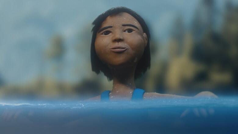 A figurine made from clay of a young girl. Her head and torso is visible as she is portrayed swimming in open water. 